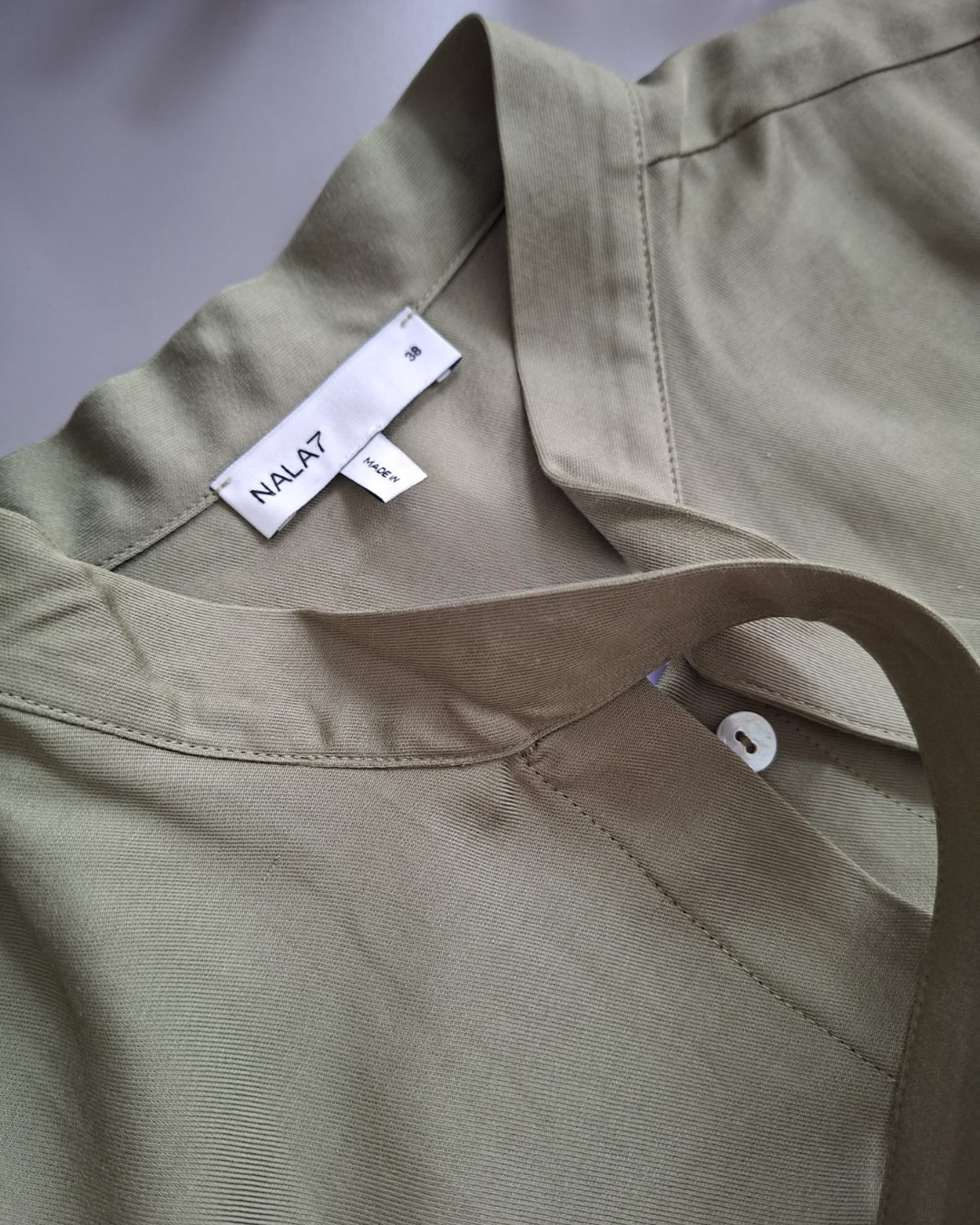 Close-up van het label, de kraag en de knoop van een groene NALA7 blouse